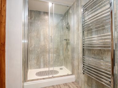 A shower enclosure with glass doors and a wall-mounted showerhead with a chrome towel radiator at Wheal Prosper@The West Dry in St Austell