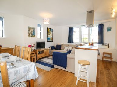 A living and dining area with a sofa a television dining table with chairs and a kitchen island stool at Broadleys Swanage