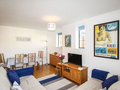 A living room with sofas a dining table with chairs a tv on a wooden stand and wall art at Broadleys in Swanage