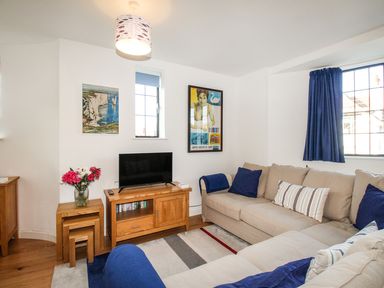 A living room with beige sofas blue cushions a wooden TV stand with a television and nested wooden tables with flowers at Broadleys in Swanage