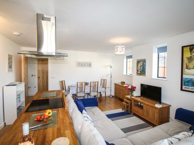 An open plan living room and kitchen with a wooden dining table chairs sofa and TV at Broadleys in Swanage