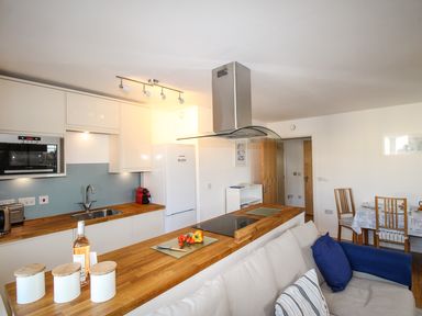 A kitchen with wooden countertops white cabinets a stove with an extractor fan a dining table with chairs and a sofa with cushions at Broadleys Swanage