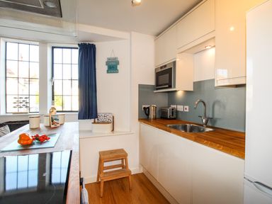 A kitchen with wooden countertops a sink microwave toaster kettle windows with blue curtains and wooden stool at Broadleys Swanage