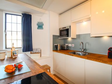A kitchen with wooden countertops a sink a microwave kettle toaster and a window with a dark curtain at Broadleys Swanage