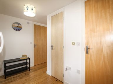 A hallway with three wooden doors a black bench with a hat on it a wall clock and a ceiling light at Broadleys in Swanage