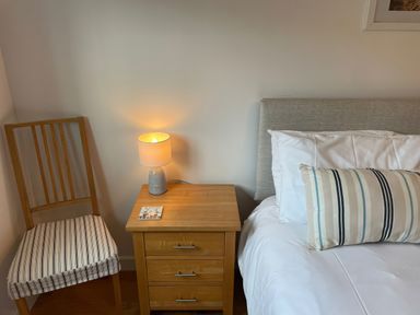 A bedroom with a bed, nightstand, lamp, chair and booklet at Broadleys in Swanage