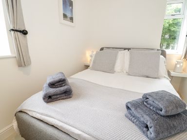 A bedroom with a double bed with gray pillows and folded towels at 1 Old Kingdom Hall in Amlwch