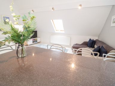 A living area with a sofa and cushions a skylight window a small television a rug and a dining table with chairs and flowers at 1 Old Kingdom Hall in Amlwch