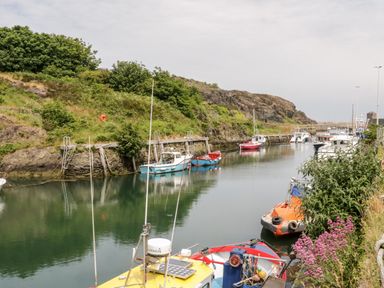 A small harbor with boats moored along a calm water channel surrounded by greenery at 1 Old Kingdom Hall in Amlwch