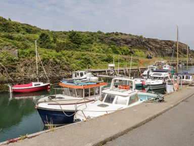 Several boats docked along a pier with a hillside covered in vegetation behind at 1 Old Kingdom Hall in Amlwch