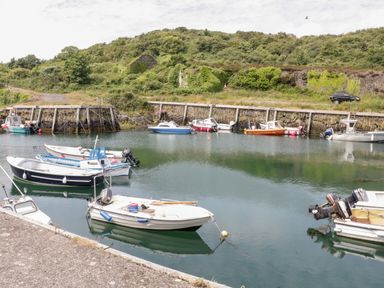 A small harbor with boats moored on calm water and greenery on a hill at 1 Old Kingdom Hall in Amlwch
