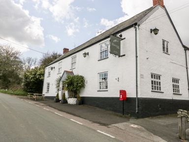 A white building with a black lower section and a hanging sign reading The Flintlock Inn with tables outside on a roadside at Red Roof in Marsh near Combe St Nicholas