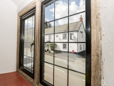 A double glazed window with black frame and stone surround looking out onto a white building with chimney and street view at Red Roof Marsh near Combe St Nicholas