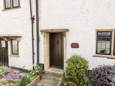 A cottage entrance with a dark wooden door surrounded by plants and flowers at Red Roof in Marsh near Combe St Nicholas