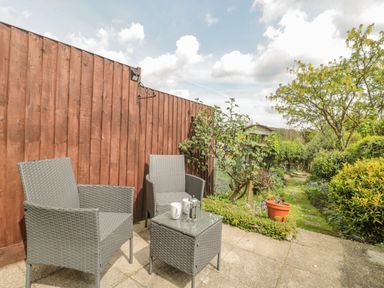 An outdoor patio with two grey wicker chairs and a small table with mugs and a French press at Red Roof Marsh near Combe St Nicholas