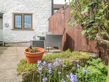 An outdoor patio area with two gray chairs a small table a terracotta plant pot with flowers and a wooden fence at Red Roof Marsh near Combe St Nicholas