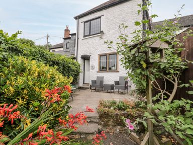 A garden with red and yellow flowers a bird feeder and patio furniture outside a white stone house at Red Roof Marsh near Combe St Nicholas