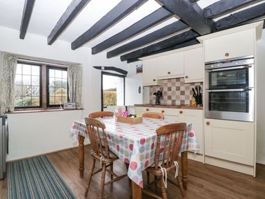 A kitchen with wooden table and chairs a polka dot tablecloth white cabinets and a double oven at Red Roof Marsh near Combe St Nicholas