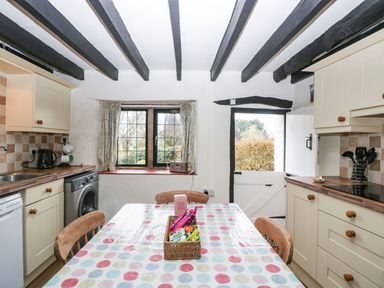 A kitchen with a dining table covered in a polka dot tablecloth and wooden chairs at Red Roof in Marsh near Combe St Nicholas