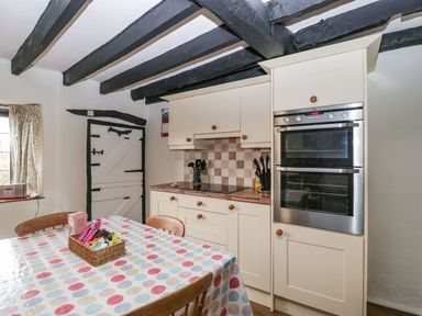 A kitchen with wooden ceiling beams a polka dot tablecloth on a table and built in ovens at Red Roof Marsh near Combe St Nicholas