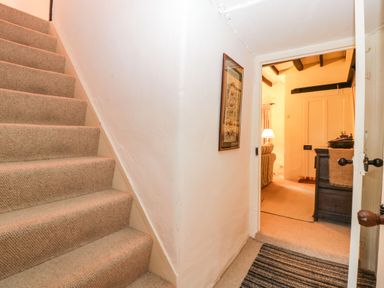 A carpeted staircase next to a hallway leading to a room with furniture and a lamp at Red Roof in Marsh near Combe St Nicholas