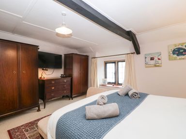 A bedroom with a bed and rolled towels a chest of drawers two wardrobes a window with curtains and paintings on the wall at Red Roof Marsh near Combe St Nicholas