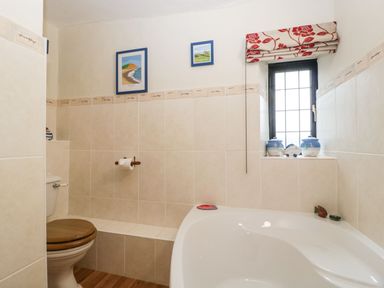 A bathroom with a toilet wooden seat a bathtub window with decorative jars and framed pictures on the wall at Red Roof Marsh near Combe St Nicholas