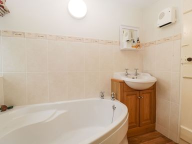 A bathroom with a bathtub a washbasin with wooden cabinet and wall-mounted heater at Red Roof Marsh near Combe St Nicholas