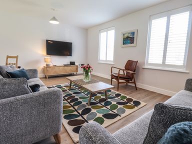 A living room with grey sofas a wooden coffee table and a wall-mounted TV at Ty Owen in Newport Pembrokeshire