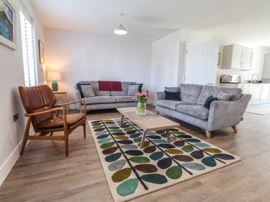 A living room with two gray sofas a brown armchair a wooden coffee table with flowers and a patterned rug at Ty Owen in Newport Pembrokeshire
