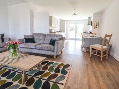 An open plan living room and kitchen with grey sofas and a wooden coffee table with flowers at Ty Owen in Newport Pembrokeshire