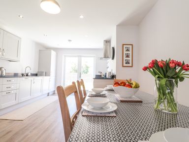 A kitchen with wooden chairs a patterned tablecloth bowls a bowl of fruit and a vase of flowers at Ty Owen in Newport Pembrokeshire
