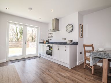 A kitchen with white cabinets a stove a clock and a dining table with a chair at Ty Owen in Newport Pembrokeshire