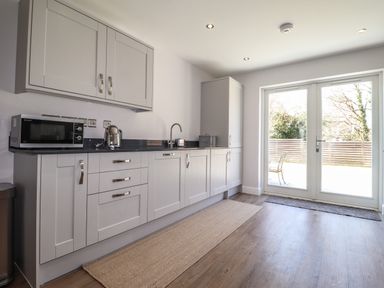 A kitchen with cabinets a microwave a kettle a sink and glass doors leading outside at Ty Owen in Newport Pembrokeshire