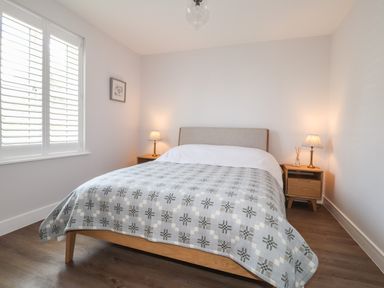 A bedroom with a bed a blanket two bedside tables with lamps and a window with shutters at Ty Owen in Newport Pembrokeshire