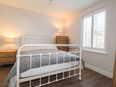 A bedroom with a white metal bed frame two wooden bedside tables with lamps a wooden chest of drawers and a window with shutters at Ty Owen in Newport Pembrokeshire