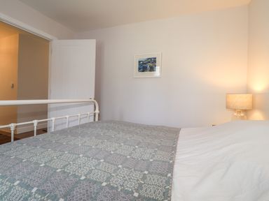 A bedroom with a bed covered by a patterned blanket a white door a lamp on a bedside table and a framed picture on the wall at Ty Owen in Newport Pembrokeshire
