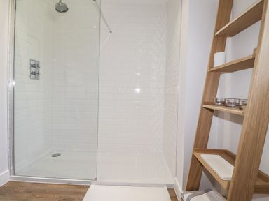 A walk in shower with glass door and a wooden shelf unit with candles and towel at Ty Owen in Newport Pembrokeshire
