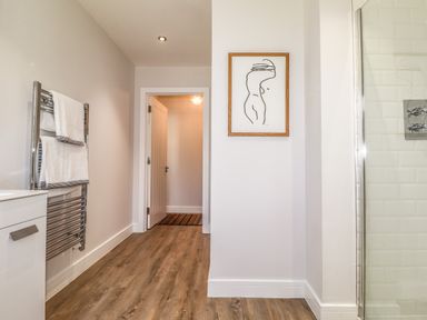 A bathroom with wooden floor a towel rack with white towels a framed line art picture and a glass shower door at Ty Owen in Newport Pembrokeshire