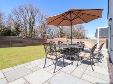 A patio with a table and umbrella surrounded by six chairs on a paved patio at Ty Owen in Newport Pembrokeshire