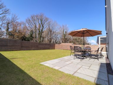 An outdoor patio with a table umbrella and chairs on a tiled area next to a grass lawn fenced by wooden panels at Ty Owen in Newport Pembrokeshire