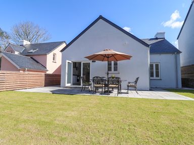 A backyard with patio furniture and an umbrella next to a white house at Ty Owen in Newport Pembrokeshire