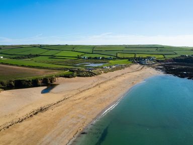 A beach with sand and sea next to green fields and scattered buildings at End Cottage in Malborough