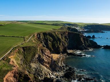 A coastal landscape with cliffs green fields and a village along the shore at End Cottage in Malborough