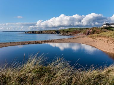 A beach with sand dunes and a curved water body reflecting clouds and blue sky at End Cottage in Malborough