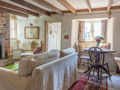 A sitting room with a sofa chair a table with flowers and exposed wooden beams at End Cottage in Malborough