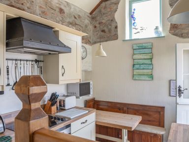 A kitchen area with a wooden bench and table a microwave and kitchen utensils at End Cottage in Malborough