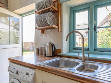 A kitchen sink with a faucet and a wooden countertop next to a washing machine and a window at End Cottage in Malborough