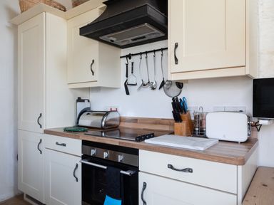 A kitchen with cream cabinets wooden countertop and various utensils at End Cottage in Malborough