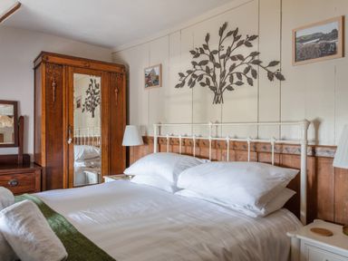 A bedroom with a white bed and pillows a wooden wardrobe with a mirrored door wall art and bedside tables with lamps at End Cottage in Malborough